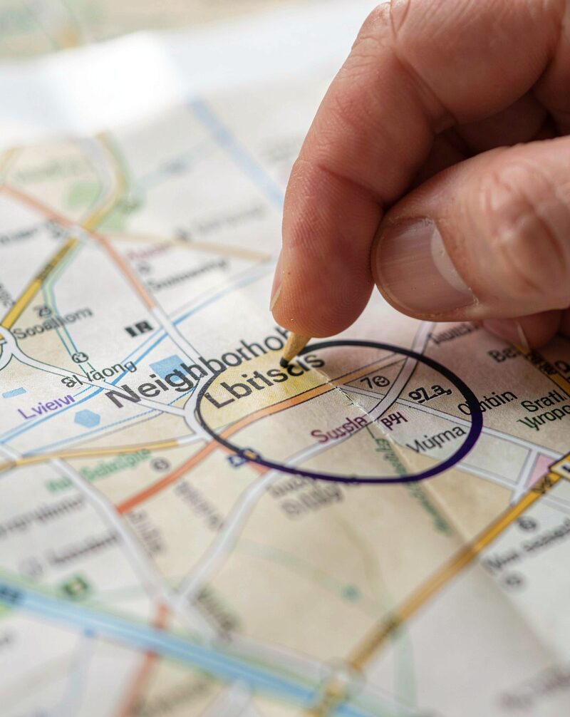 A paper city guide and a folded transit map on a kitchen table beside a set of new keys, a coffee cup, morning light, boxes half unpacked behind